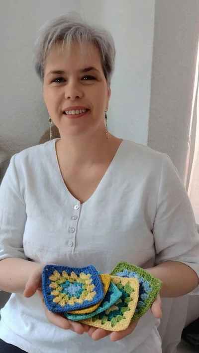 La Profe Anita, maestra crochetera, sonriendo y mostrando varios grannys tejidos en sus manos